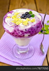 Dessert milk with blueberry, cornflakes, curd, spoon in a glassware on a purple napkin on a wooden boards background