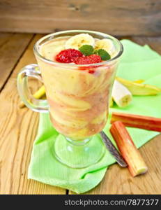 Dessert milk with curd, banana, strawberries and rhubarb, spoon, a green napkin on background wooden plank