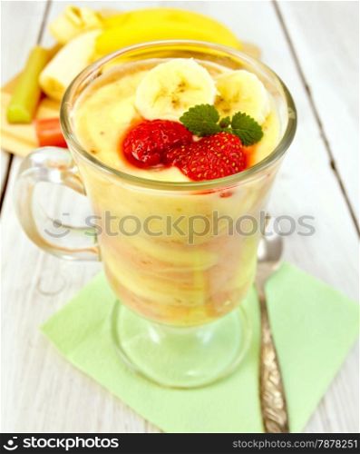 Dessert milk with curd, banana, strawberries and rhubarb, spoon on a green paper napkin on the background light wooden boards