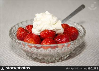 Dessert of fresh strawberries with whipped cream in a glass bowl