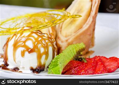 Dessert of pancake with banana, ice-cream, caramel, strawberry and mint
