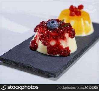 dessert panacotta with raspberry jam and oranges on a black surface, close up