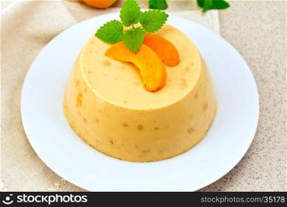 Dessert panna cotta cheesecake with apricots in a white plate, mint on a napkin on the background of a brown granite table