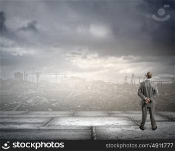 Destruction concept. Rear view of businessman looking at ruins of city