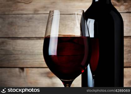 Detail of a glass red wine with a bottle on a wooden background