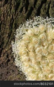 Detail of a white floral arrangement with white roses near a tree