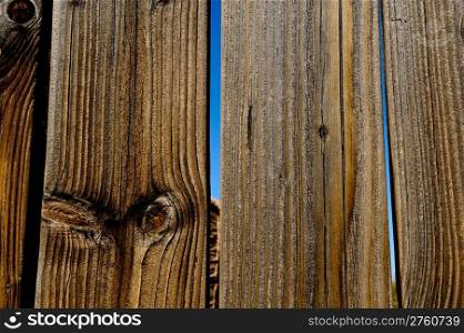 Detail of an old wood fence. A blue sky is through the gap between the planks.. Commercial Photography