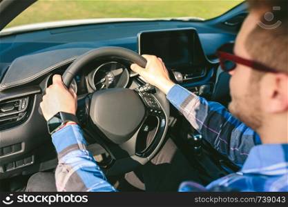 Detail of arms of young man holding the steering wheel while driving the car. Young man holding steering wheel while driving the car