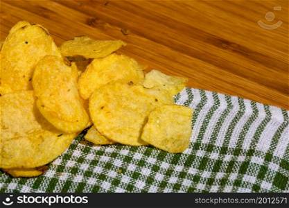 Detail of crispy potato chips on napkin on wooden table. Salted potato chips, junk food concept