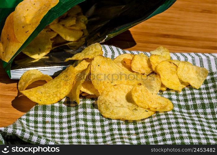 Detail of crispy potato chips on napkin on wooden table. Salted potato chips, junk food concept