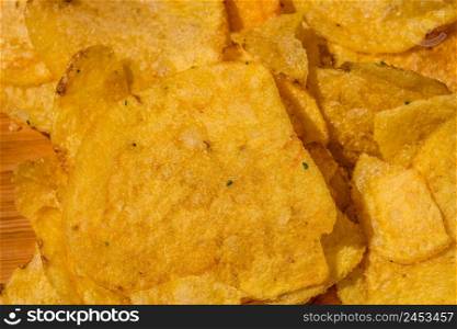 Detail of crispy potato chips on wooden table. Salted potato chips, junk food concept
