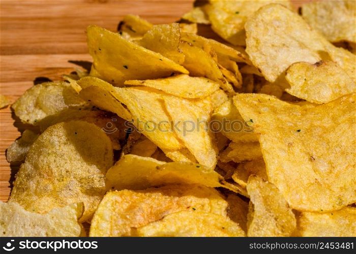 Detail of crispy potato chips on wooden table. Salted potato chips, junk food concept