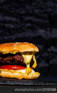 Detail of fresh tasty beef cheeseburger with melted cheese isolated on black background