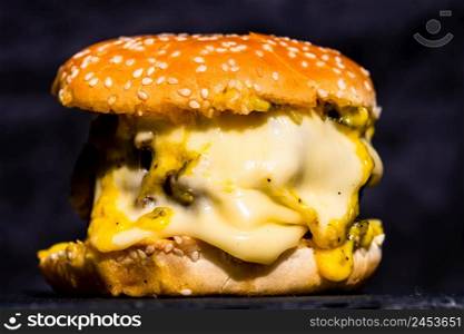 Detail of fresh tasty beef cheeseburger with melted cheese isolated on black background