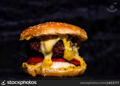 Detail of fresh tasty beef cheeseburger with melted cheese isolated on black background