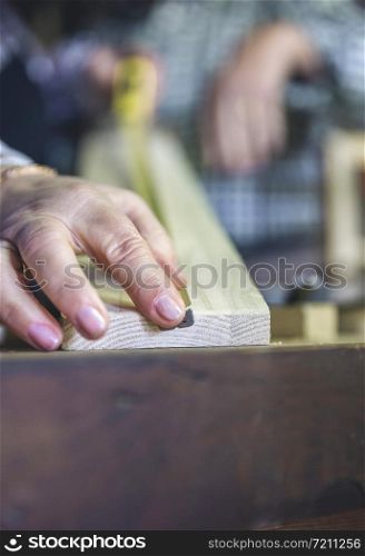 Detail of hand of senior carpenter measuring in a carpentry workshop. Selective focus on man in background. Carpenter&rsquo;s hand measuring in a carpentry