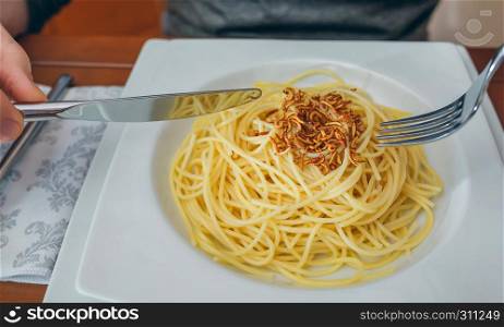 Detail of hands of unrecognizable man eating spaghetti with crispy worms. Hands of man eating spaghetti with worms