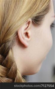 Detail of the head with female human ear and blonde braid hair, close up. Close up on female ear and braid hair