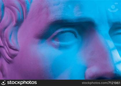 Detail of toned gypsum copy of ancient statue of Guy Julius Caesar Octavian Augustus head for artists on a black background. Close up view on eye. Blue and pink toned.. Close up detail of gypsum copy ancient statue Augustus head isolated on black background. Plaster sculpture man face.