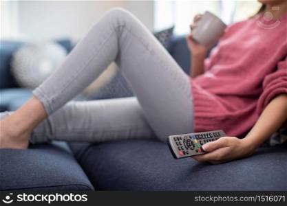 Detail Of Woman Relaxing On Sofa Holding Remote Control And Watching Television