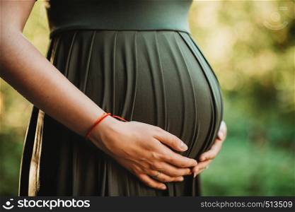 detail of womans hands holding pregnant belly expecting birth of baby soon