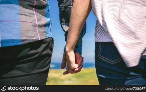 Detail of young unrecognizable couple holding hands outdoors. Unrecognizable couple holding hands