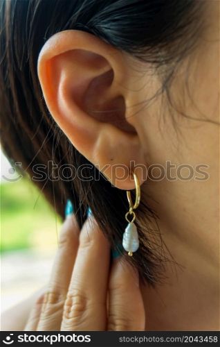 Detail of young woman wearing beautiful golden earring white pearl. Women accessories. Selective focus.
