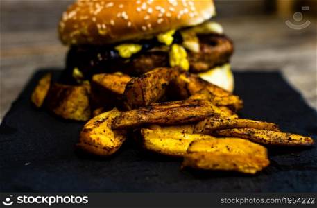 Detail view of fresh tasty cheese burger and fried potatoes on a wooden table