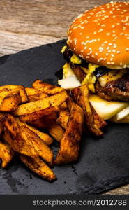 Detail view of fresh tasty cheese burger and fried potatoes on a wooden table