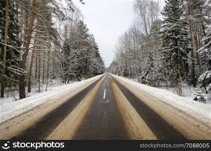 details of the snow-covered road in the winter, traces of cars and tracks from transport, along the roadway grows a forest with trees. details of the snow-covered road in forest
