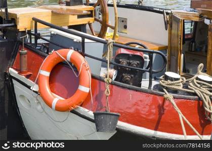 Details of the stern of an old flatbottom boat, with a buoy, bucket, anchor winch, ridder, pump and ropes