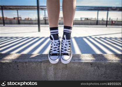 Details of woman legs standing on concrete ledge in her classic sneakers