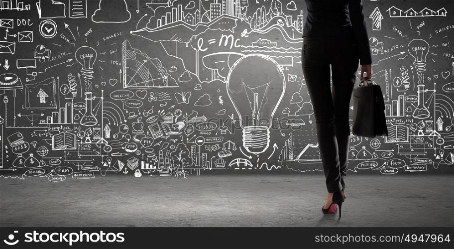 Determined and goal oriented. Rear view of businesswoman with suitcase looking at business ideas on wall