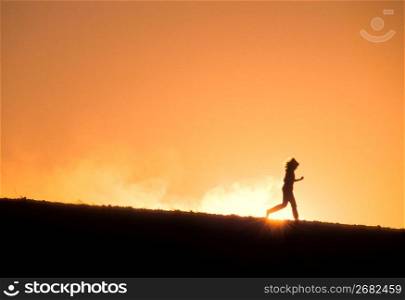 Determined, athletic runner running downhill against sunset in remote area