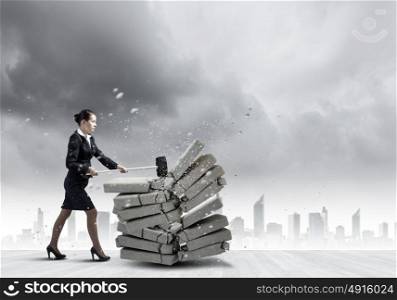 Determined business lady. Young angry businesswoman crashing bricks with hammer