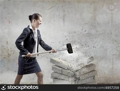 Determined business lady. Young angry businesswoman crashing bricks with hammer