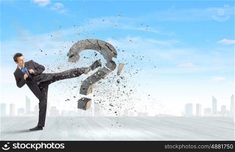 Determined businessman. Businessman breaking stone question mark with karate kick