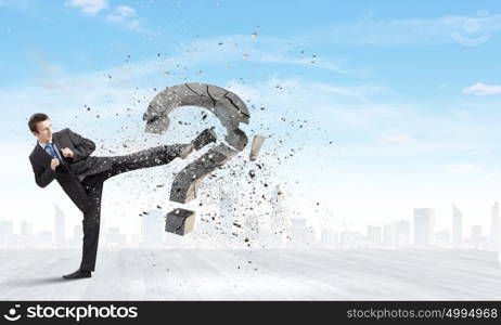 Determined businessman. Businessman breaking stone question mark with karate kick