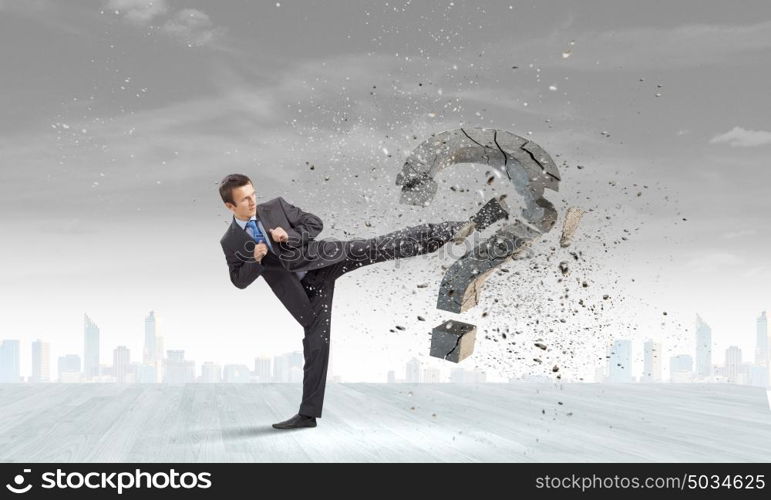 Determined businessman. Businessman breaking stone question mark with karate kick