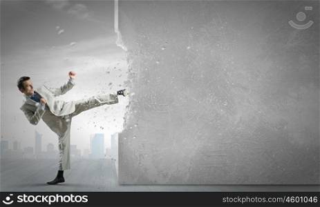 Determined businessman. Businessman breaking stone wall with karate kick