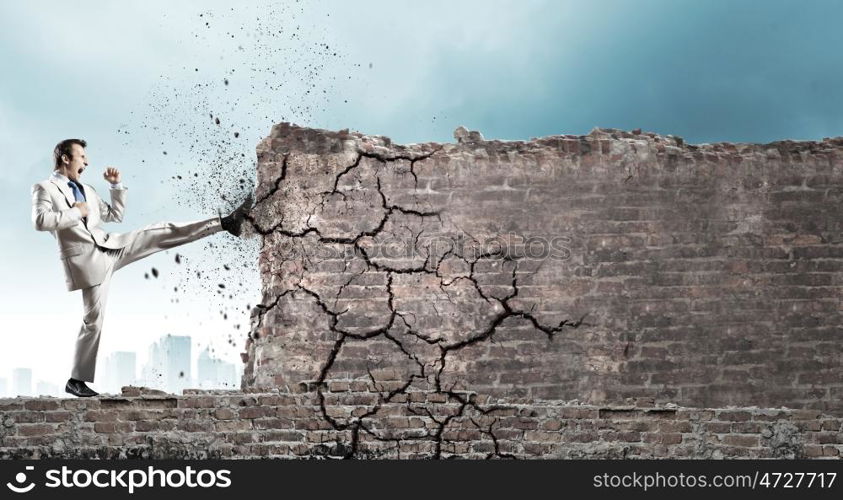 Determined businessman. Businessman breaking stone wall with karate kick