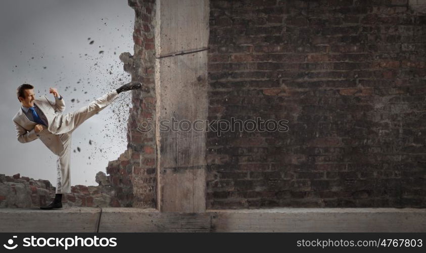 Determined businessman. Businessman breaking stone wall with karate kick