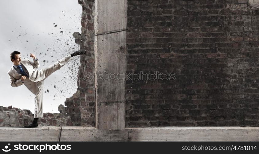 Determined businessman. Businessman breaking stone wall with karate kick