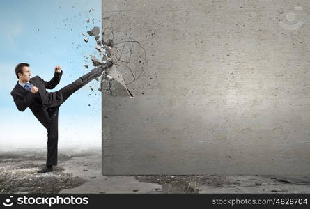 Determined businessman. Businessman breaking stone wall with karate kick