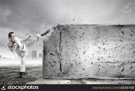 Determined businessman. Businessman breaking stone wall with karate kick