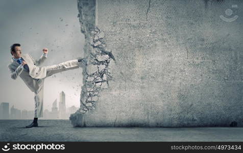 Determined businessman. Businessman breaking stone wall with karate kick