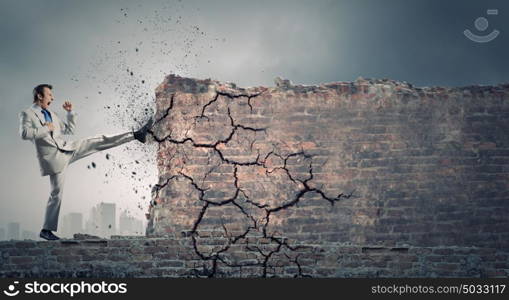 Determined businessman. Businessman breaking stone wall with karate kick