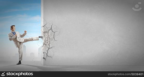 Determined businessman. Businessman breaking stone wall with karate kick