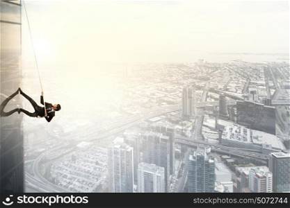 Determined businessman climbing building with help of rope. Getting to top