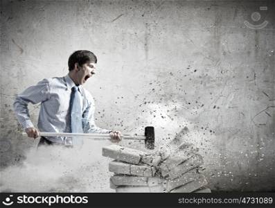 Determined businessman. Young angry businessman crashing bricks with hammer